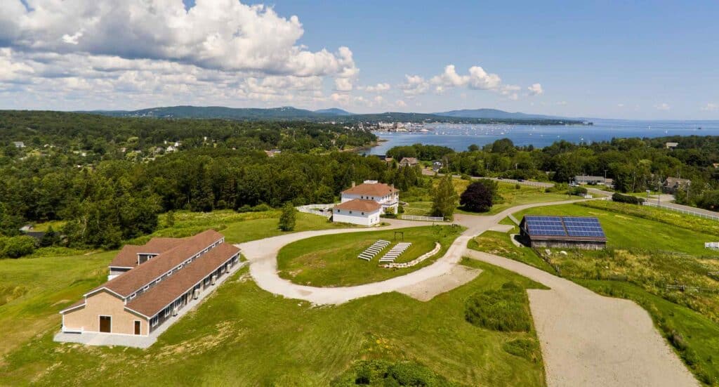 Rockland Maine Wedding Venues A large green field with buildings and trees and water in the background.