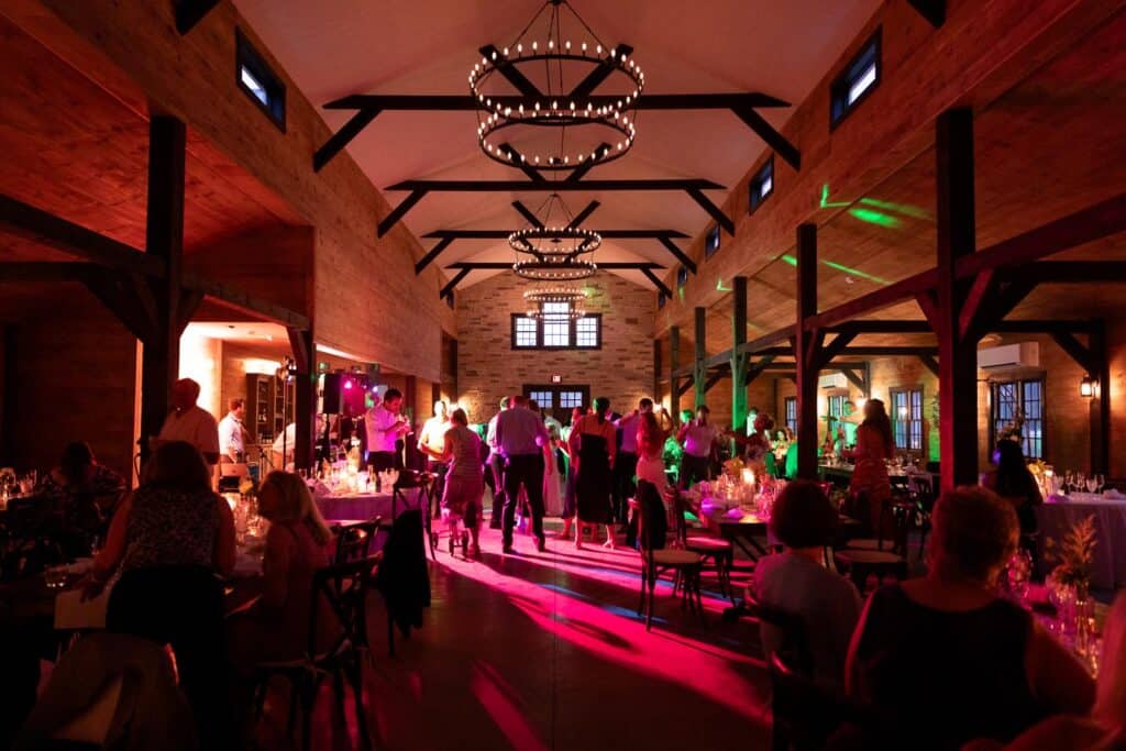 Rockland Maine Wedding Venues Elegant reception at Ash Point Estate with dim lighting, guests dancing, and large chandeliers overhead.