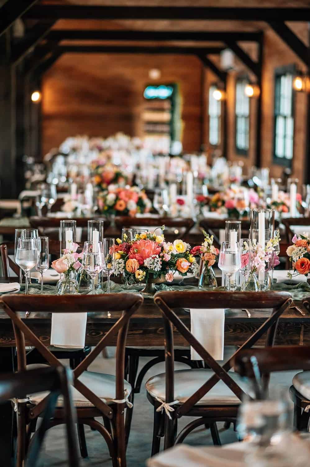 Elegant reception setup in a rustic venue with wooden beams, and long tables with floral centerpieces and glassware.