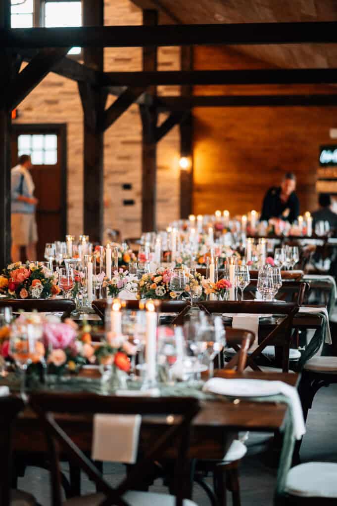 4 Steps To Plan A Luxury Wedding Weekend In Maine 2 Luxury wedding weekend in maine, elegant wedding reception with floral centerpieces on wooden tables, candles, and guests in the background in a rustic venue.