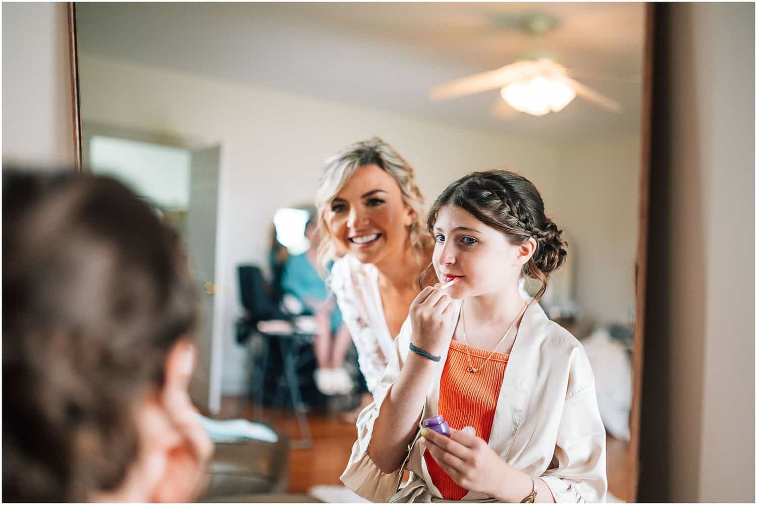 A bride watching her flower girl apply lip gloss.