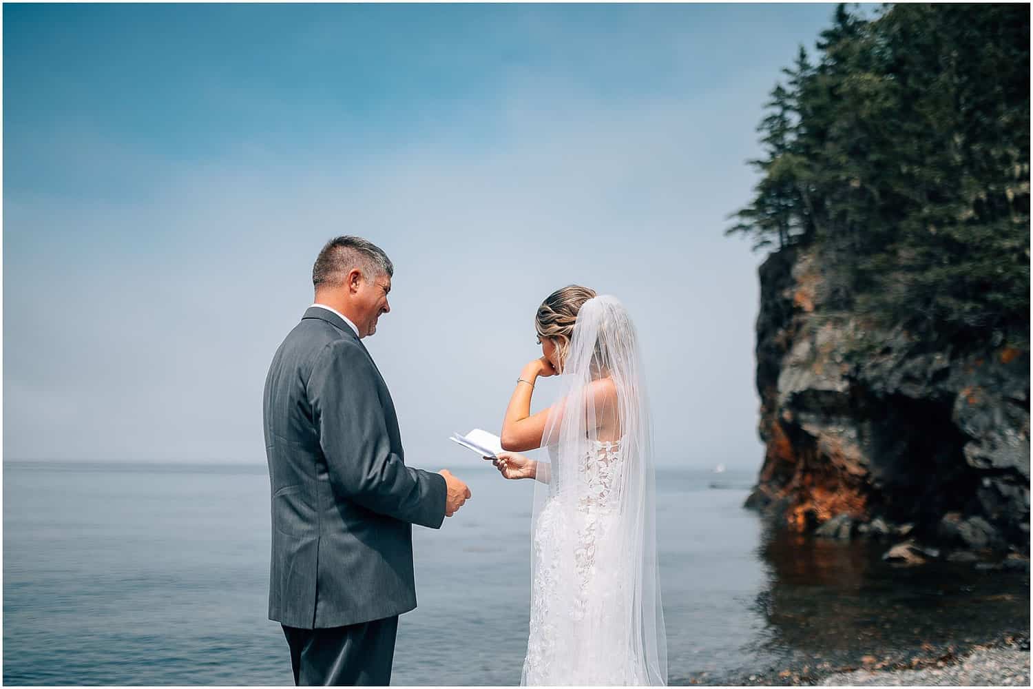 A bride and groom reading vows in front of the water.