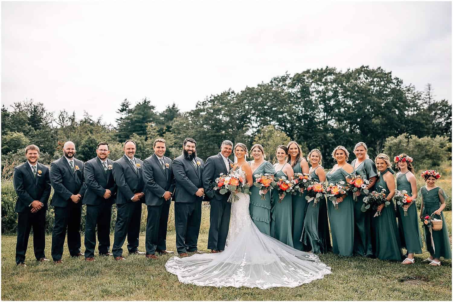 Formal portrait of a wedding party, standing in a field.