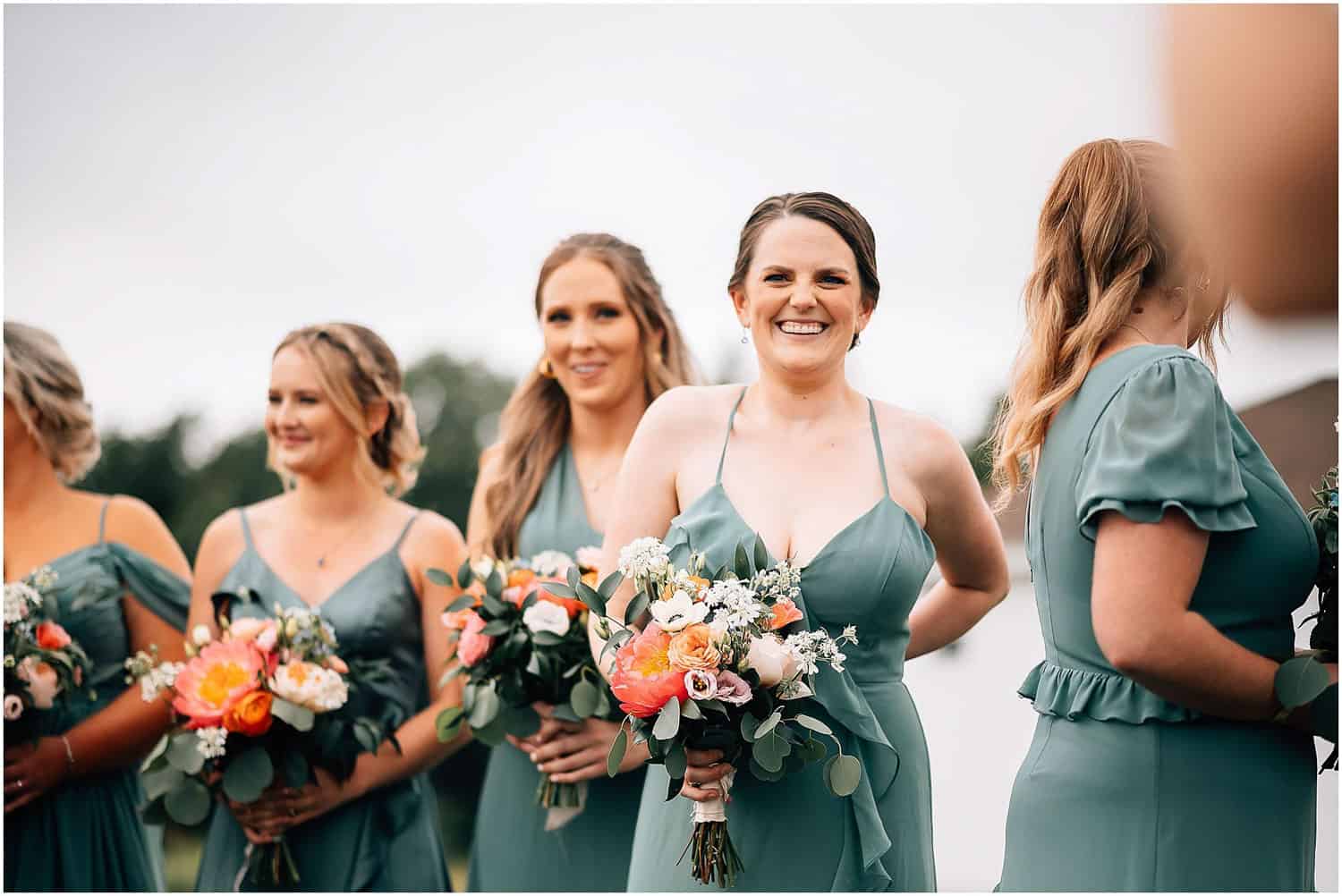 Bridesmaids in green dresses, holding bouquets and laughing.