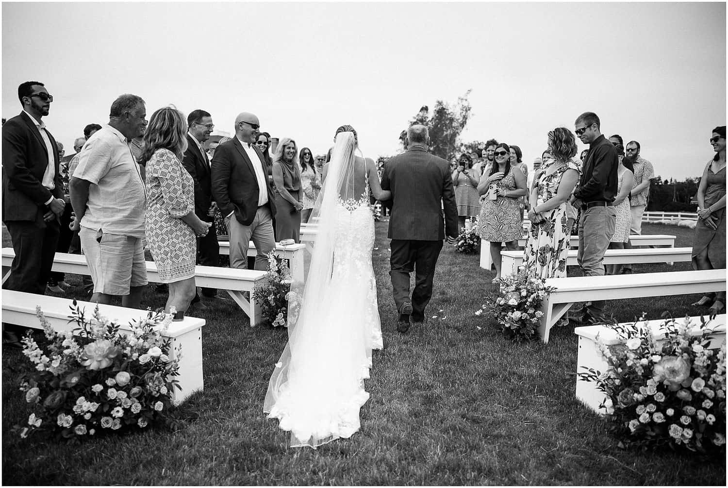 A bride and her father walking down the aisle in an outdoor ceremony.