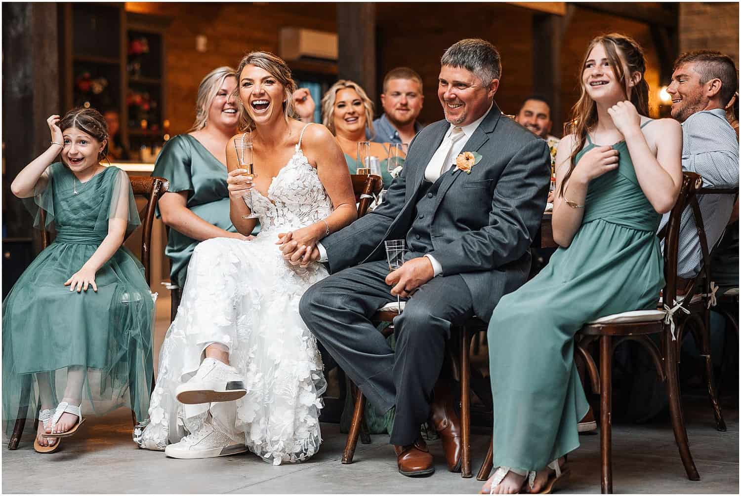 A bride and groom laughing, surrounded by the wedding party and guests.
