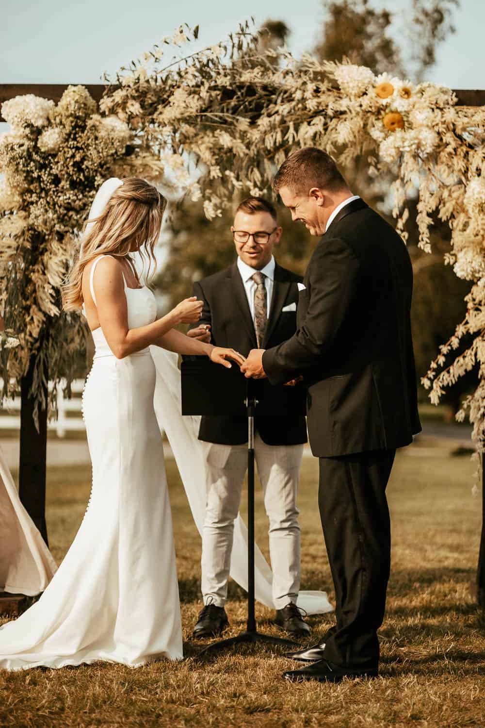 A bride and groom exchanging their wedding rings with a preacher.