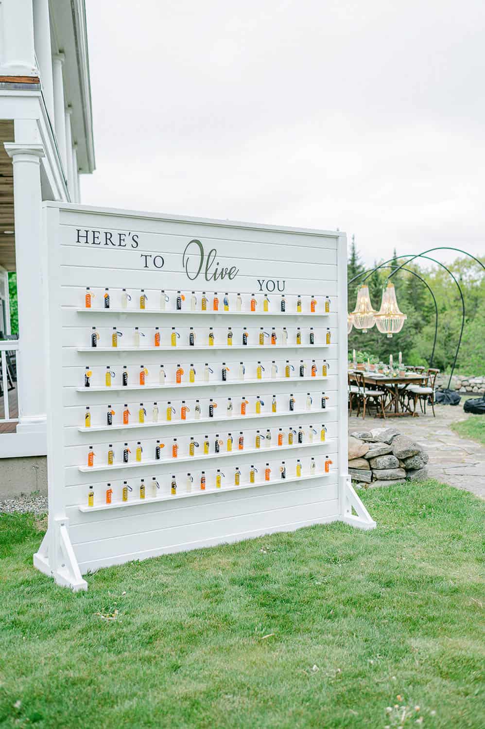 A white display board with rows of bottles on it and decorative text on it that reads, "here's to olive you".