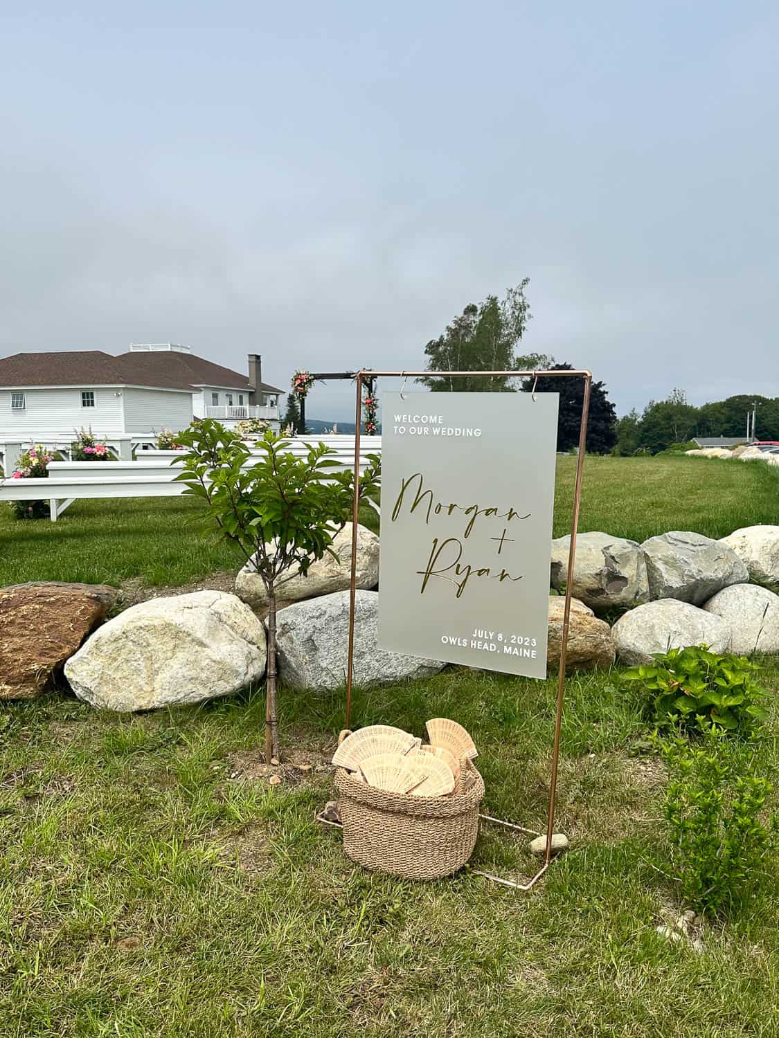 A "Welcome to Our Wedding" sign posted in a yard with decorative rocks around it.