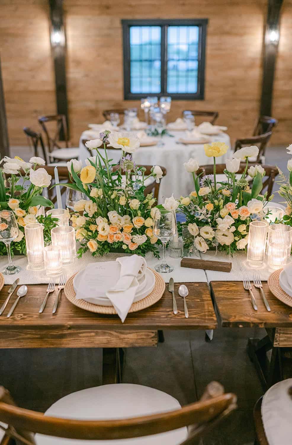 A wedding reception table set with yellow and white flowers and candles.