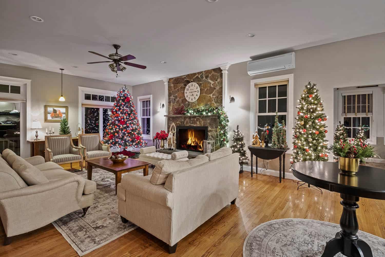 Elegant living room at ash point estate decorated for christmas with multiple trees, a lit fireplace, and cozy furnishings.