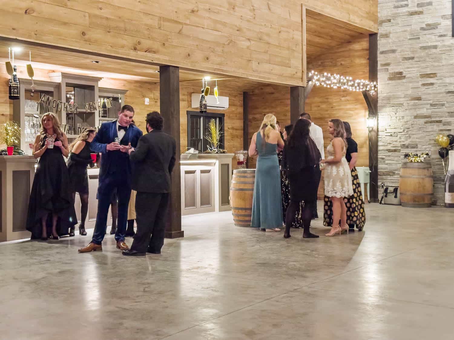 People socializing at Ash Point Estate with elegant attire, held in a room featuring wood and stone accents and string lights.