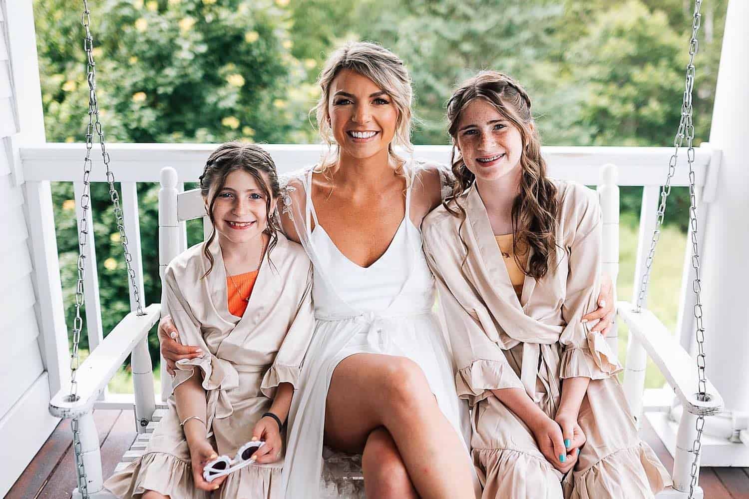 Three smiling females in matching robes sitting on a porch swing at Ash Point Estate.