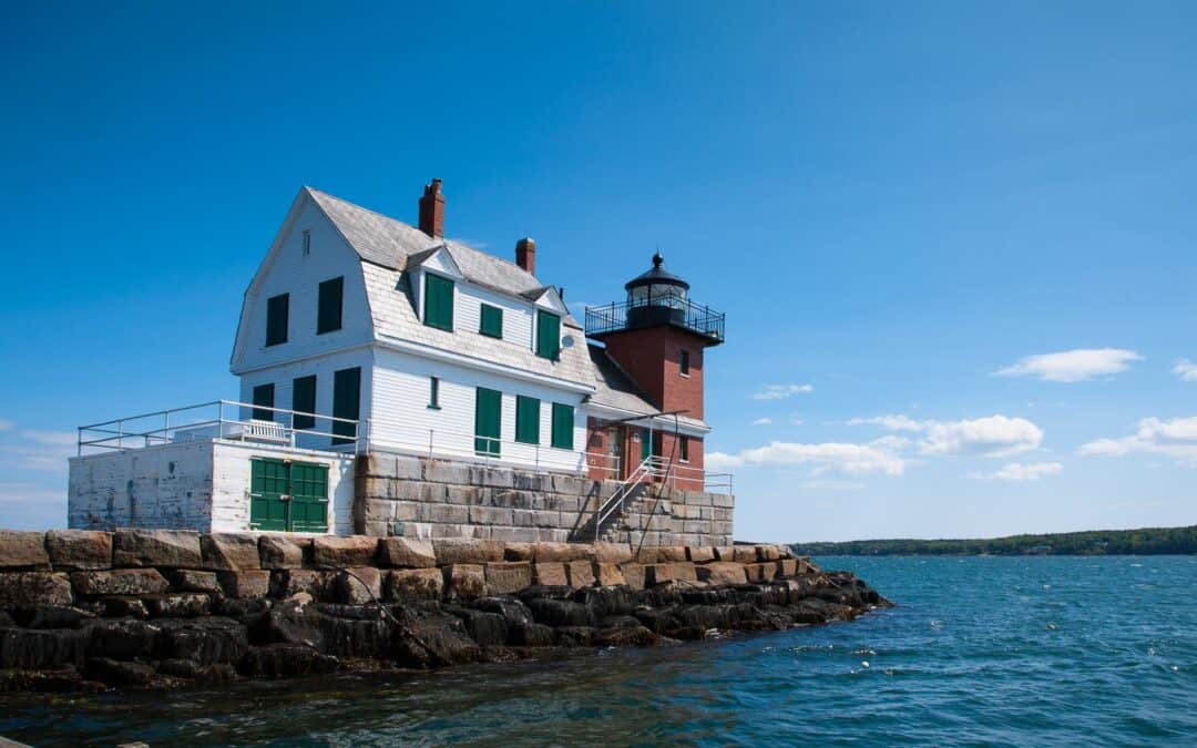 Rockland Breakwater lighthouse with its wooden building and brick tower, sits on the end of a breakwater on a summer day.