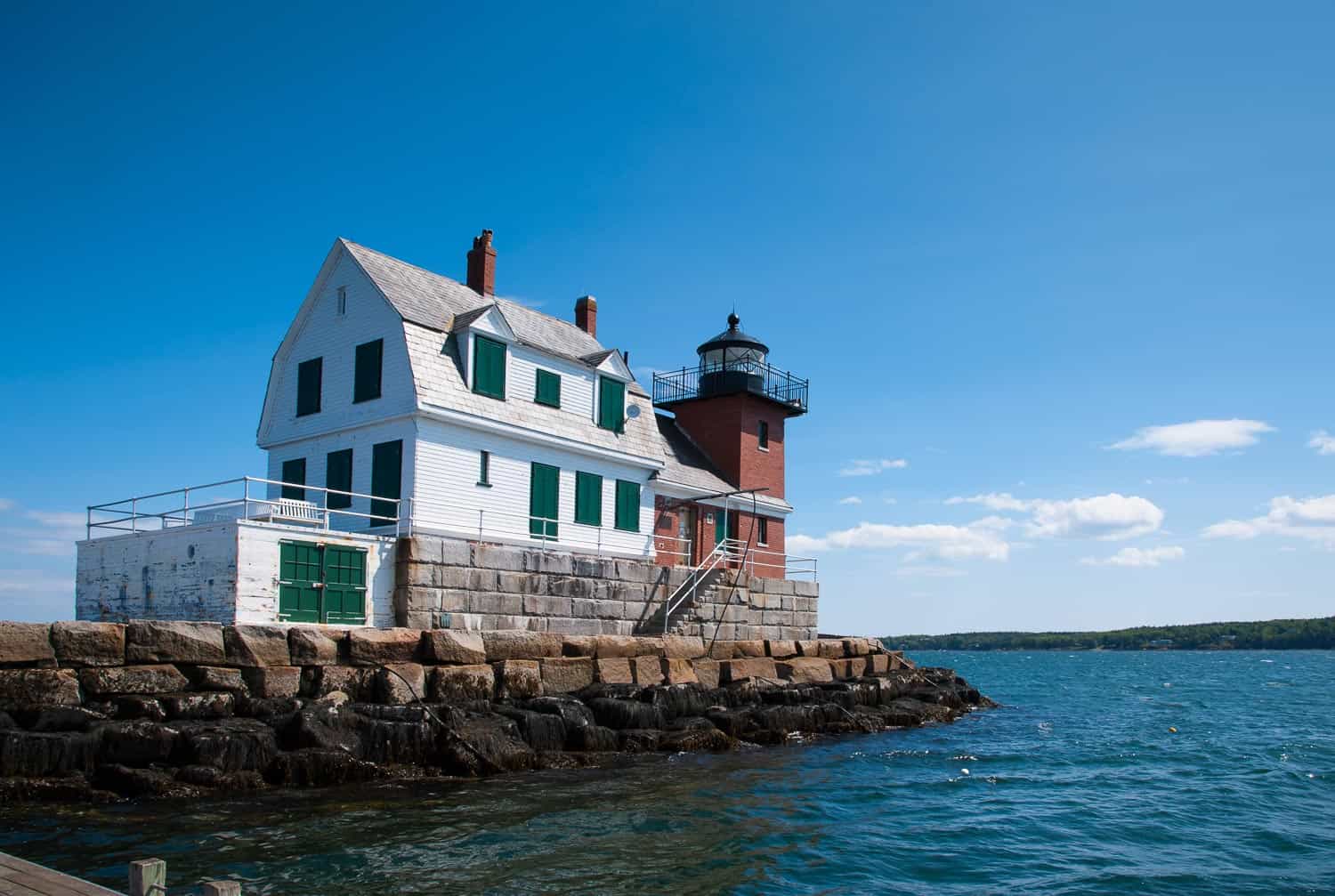 Rockland Breakwater lighthouse with its wooden building and brick tower, sits on the end of a breakwater on a summer day.