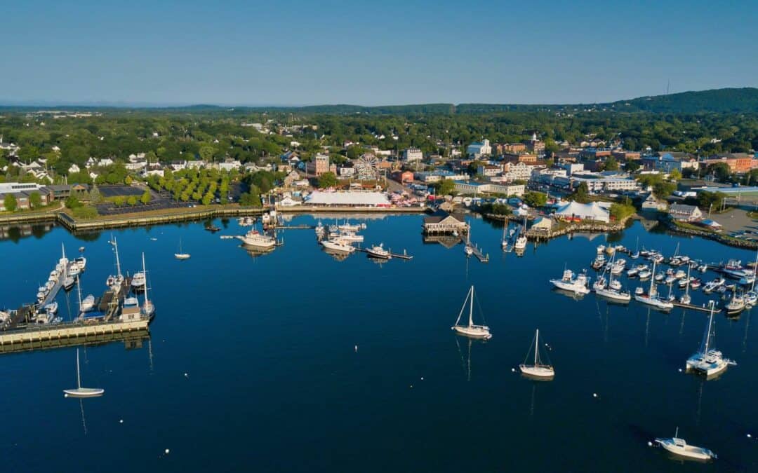Aerial view of Maine's Rockland Harbor with a marina full of boats, surrounded by green hills and residential areas.