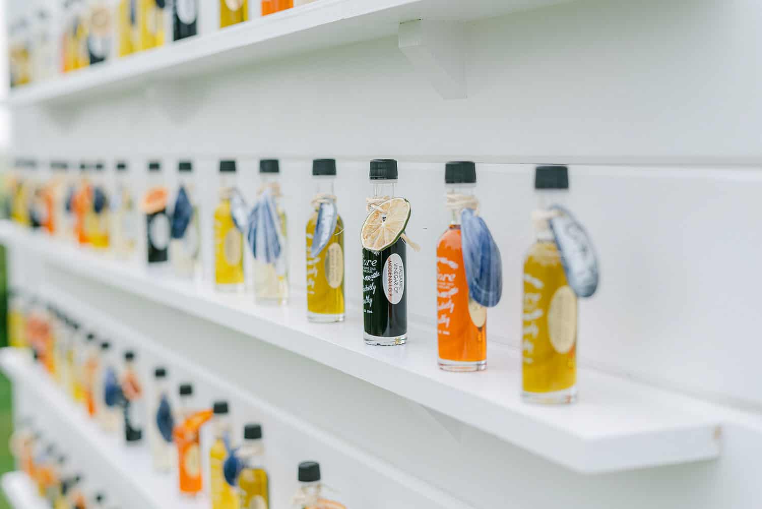 Rows of colorful vinegar bottles, prominently displayed on white shelves, with a focus on a bottle with a lime slice.