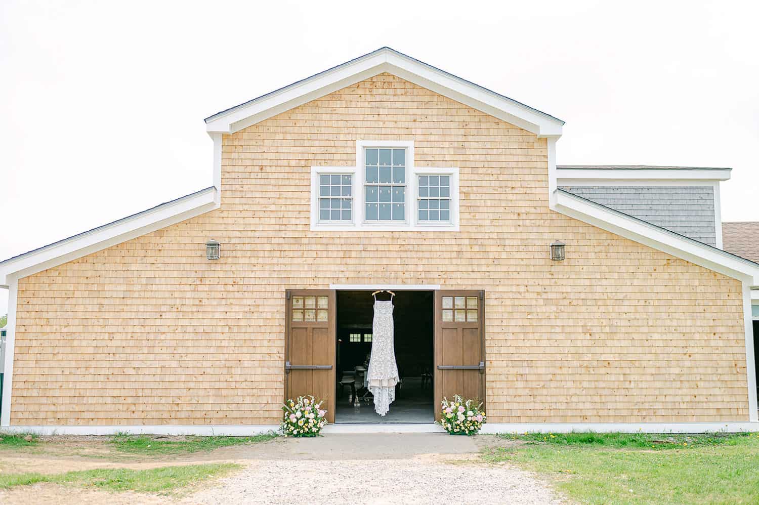 A wedding dress hanging in the open doorway of a barn styled with light wood siding, under a clear sky.