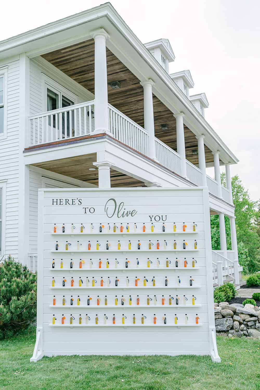 A white display board with rows of bottles on it and decorative text on it that reads, "here's to olive you".
