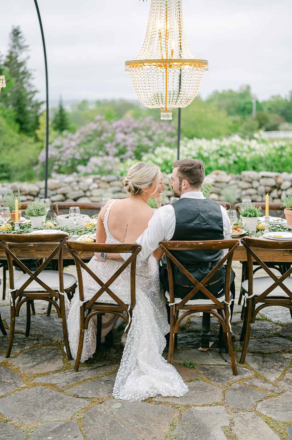 A bride and groom seated at a beautifully set wedding table outdoors, sharing an intimate moment.