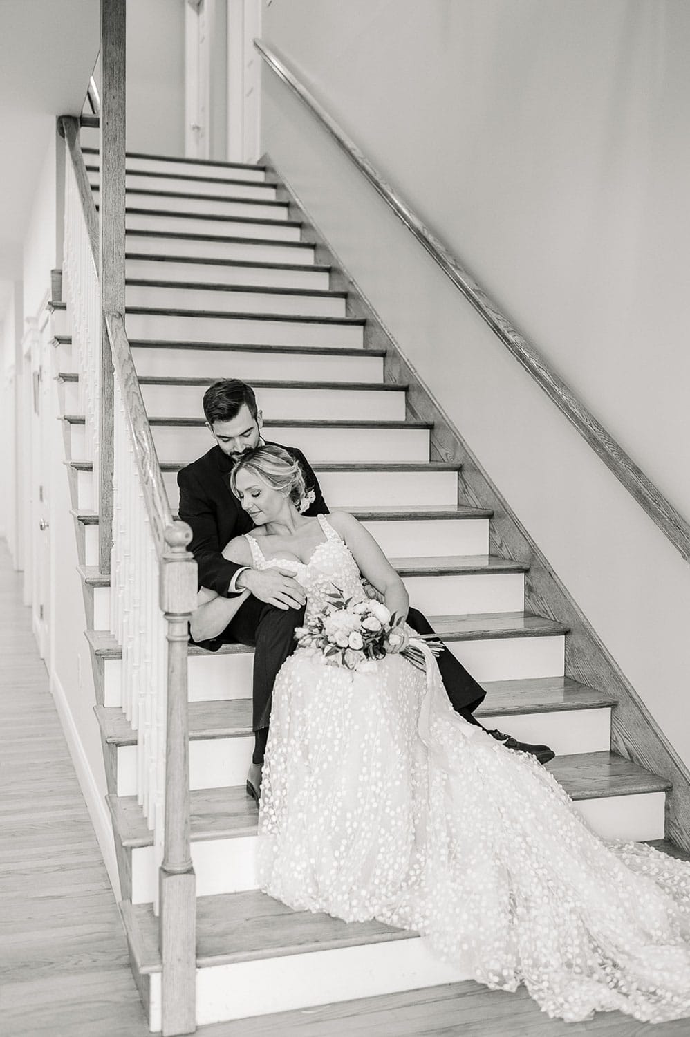 A bride and groom sitting on a staircase, the bride resting her head on the groom's shoulder.