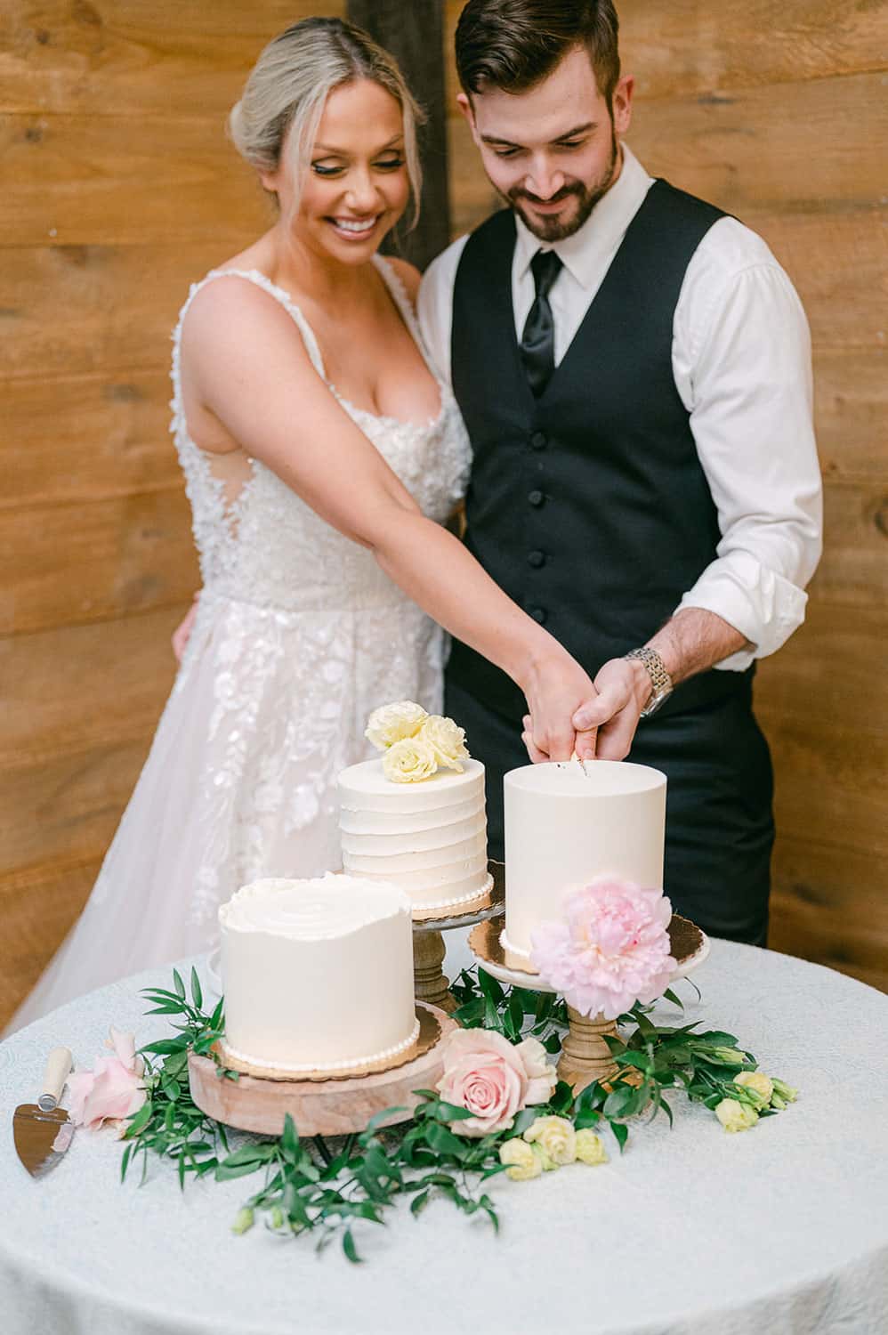 A bride and groom cutting a three-tiered wedding cake adorned with fresh flowers on a table.