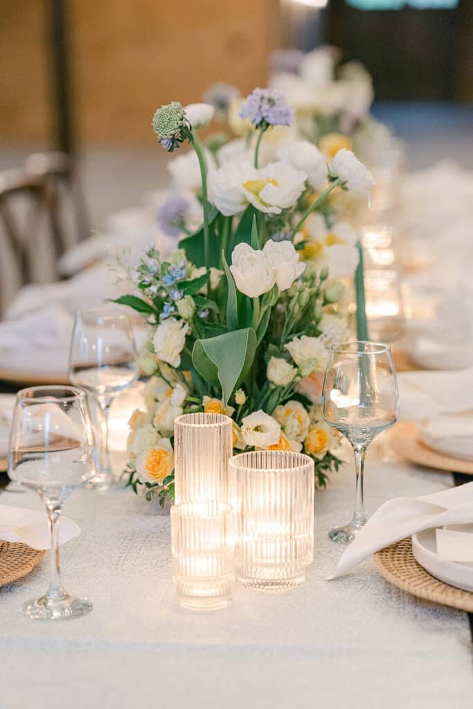 Maine coastal luxury wedding venues, reception table with floral arrangements, white tulips, yellow roses, candles in glass holders, and crystal wine glasses.