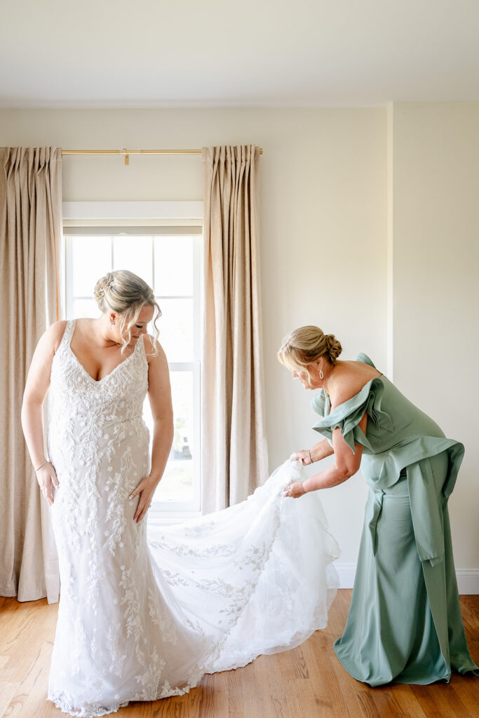 Mother of bride helps bride get ready for wedding ceremony, lifting train off floor