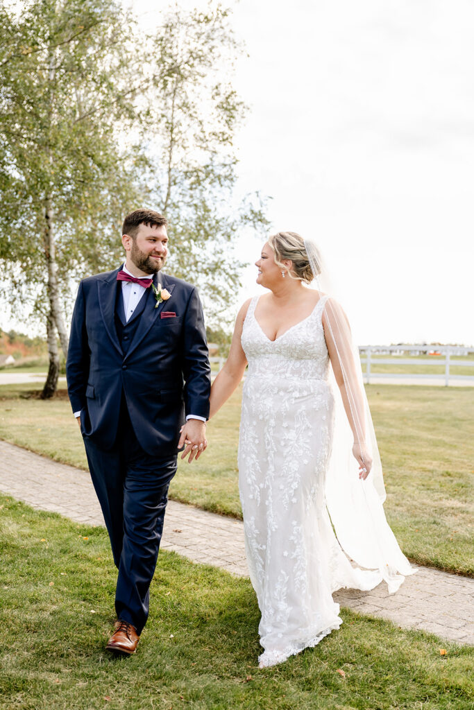 Bride and groom walk holding hands, smiling at each other at ash point estate